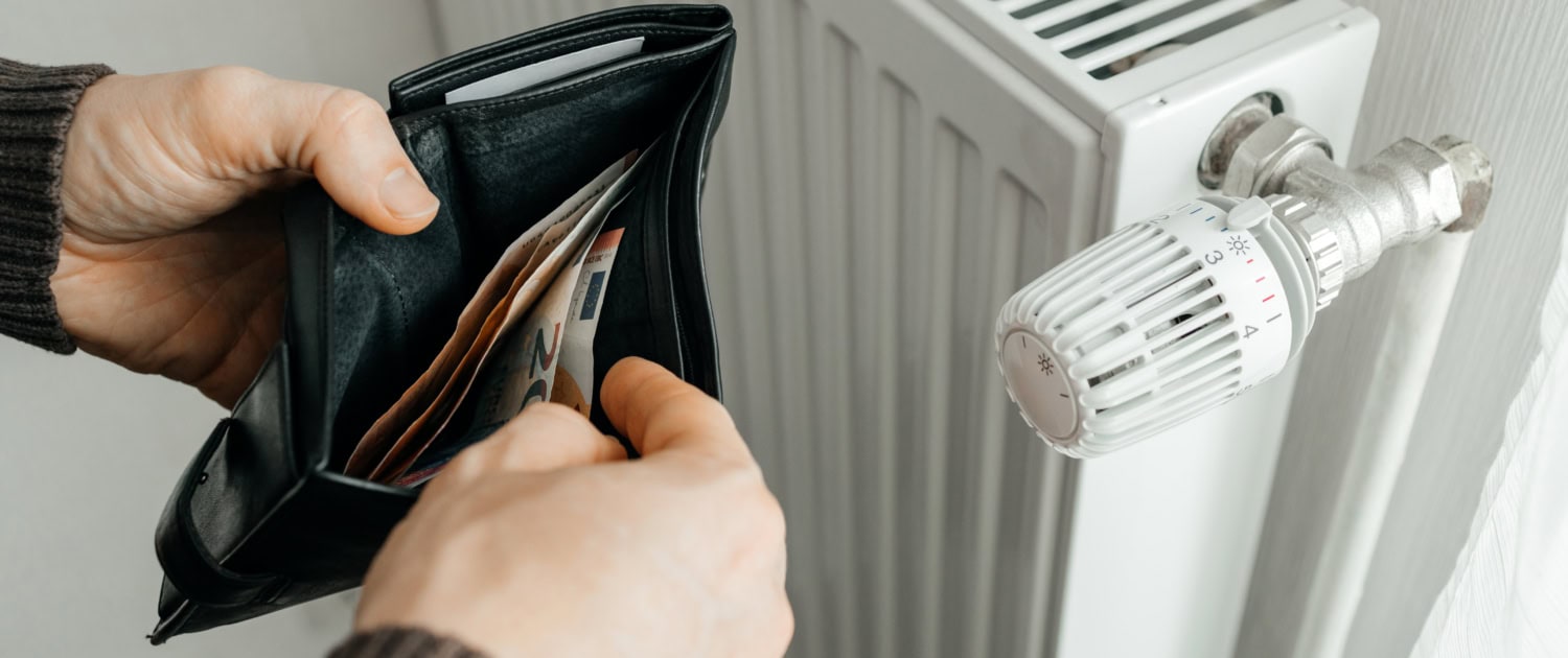 A man holds a wallet with banknotes of money inside next to a heating radiator. Rising prices for heating and natural gas. Energy Crisis in Europe