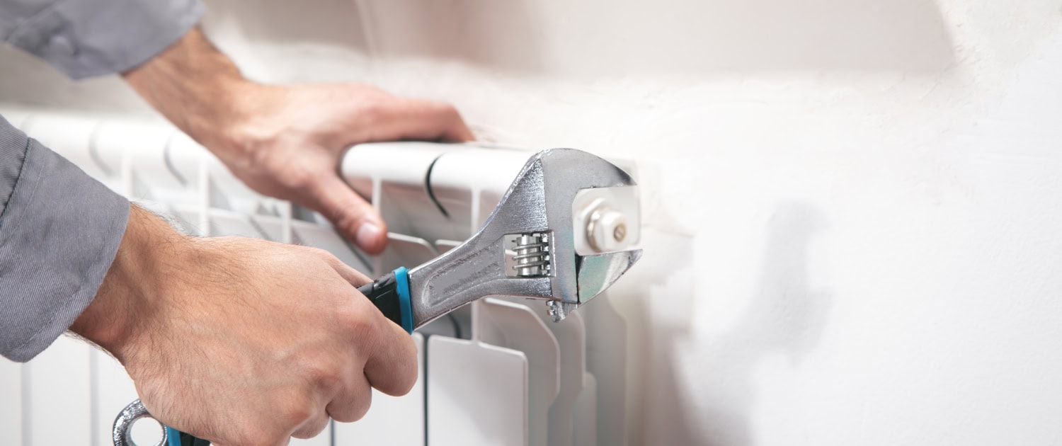 Man repairing radiator with adjustable wrench.