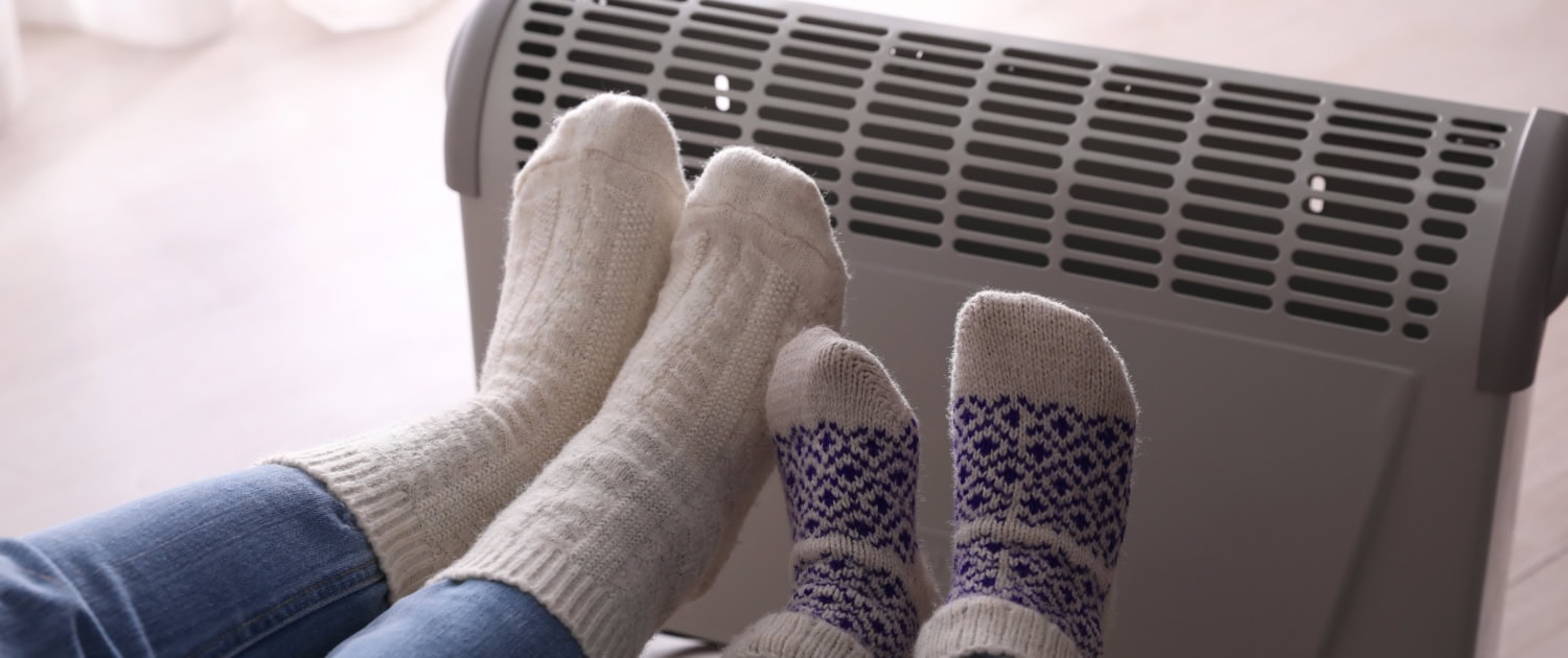 Mother and child warming feet near electric heater at home, closeup