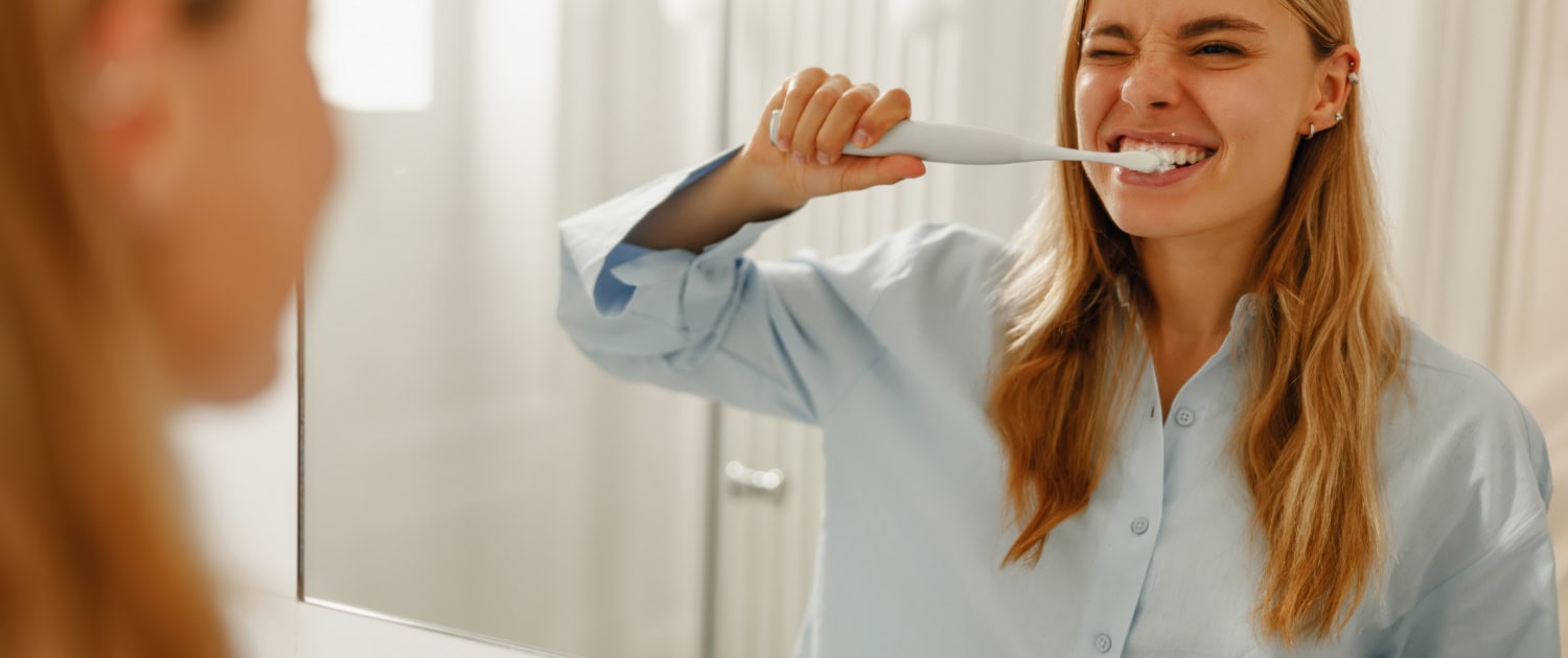 Morning Routine A Woman Happily Brushing Her Teeth in Front of a Bathroom Mirror